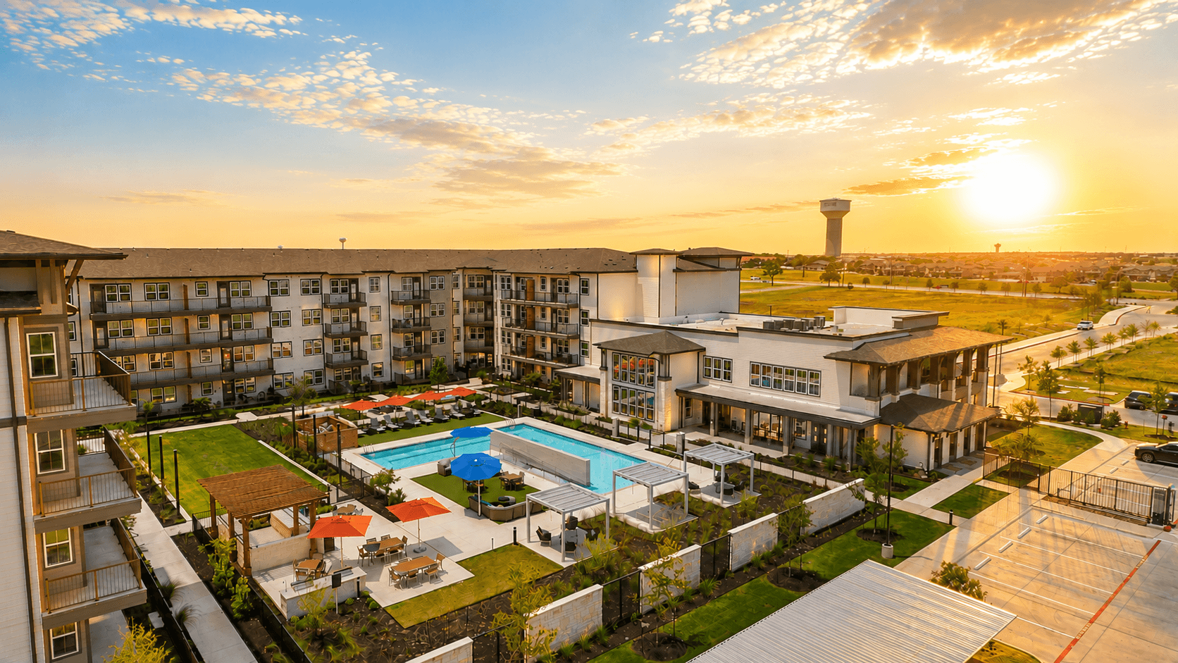 A sunset view of a large apartment complex with a pool and a tower in the distance.